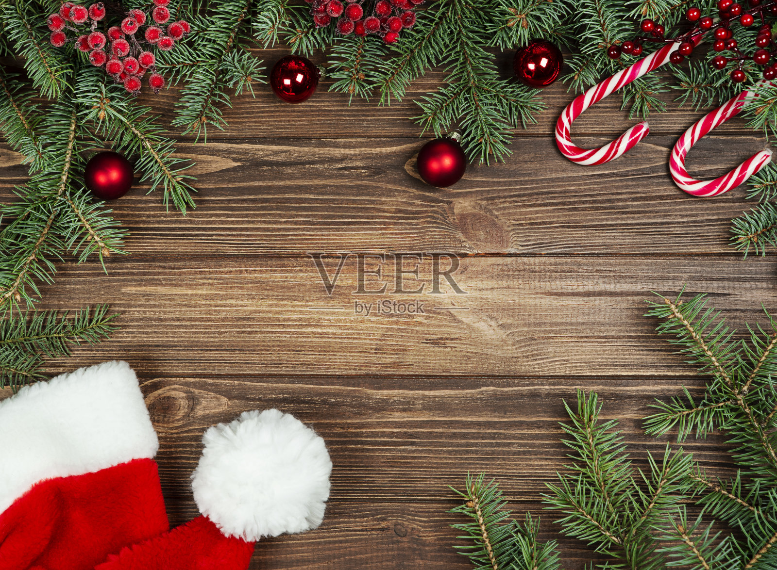 圣诞明信片:冷杉树枝，棒棒糖，圣诞帽，木制背景上的红球。照片摄影图片