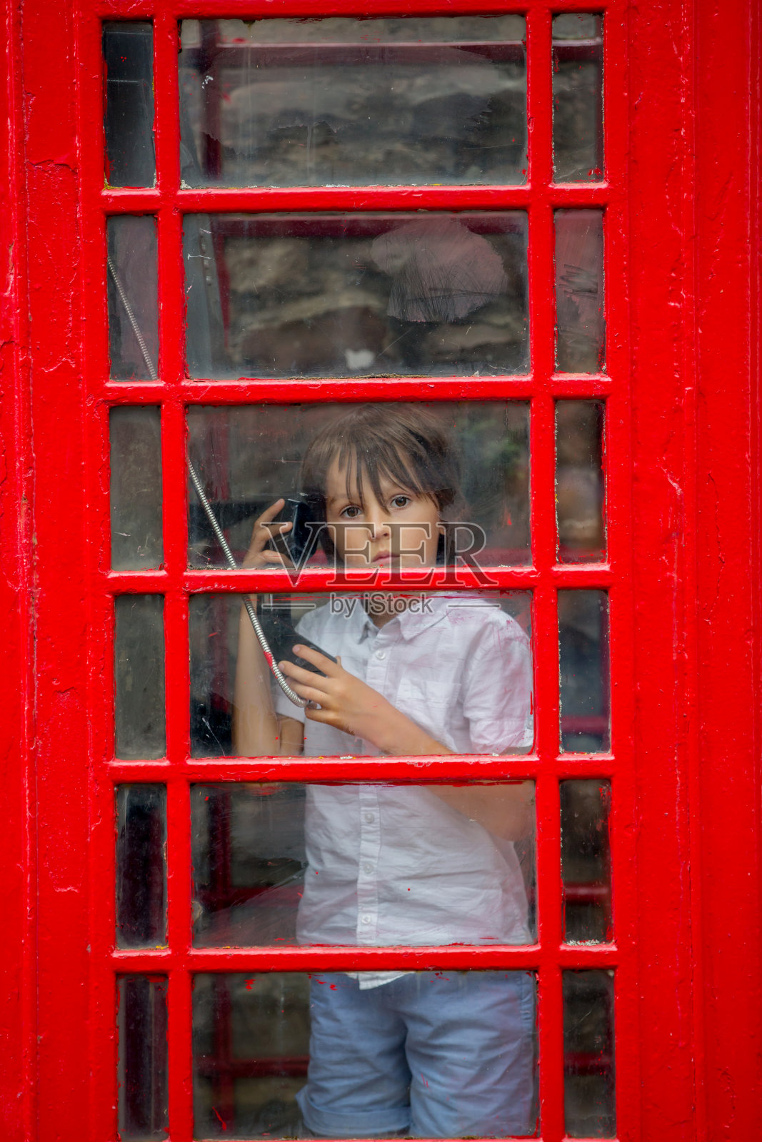 可爱的男孩，孩子，在城市里的一个红色电话亭里打电话照片摄影图片