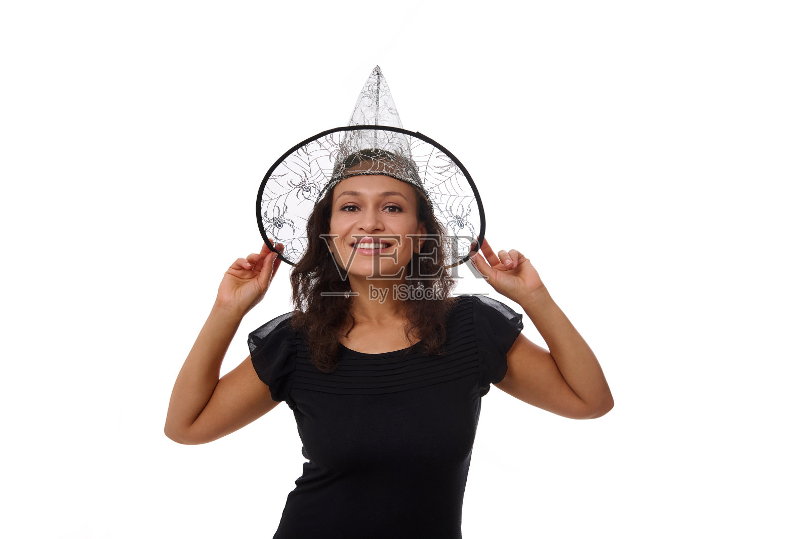 孤立的肖像在白色背景与复制空间为万圣节广告的一个迷人的年轻女子微笑着美丽的牙齿微笑，戴着女巫巫师的帽子，看着相机照片摄影图片