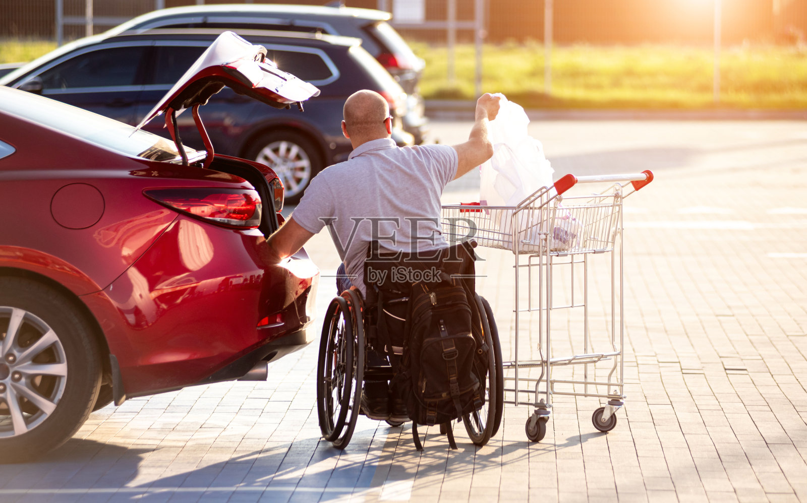 一个身体残疾的人把买的东西放在超市停车场的汽车后备箱里照片摄影图片
