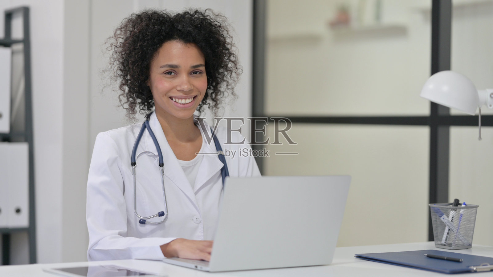 非洲女医生一边用笔记本电脑工作一边微笑照片摄影图片