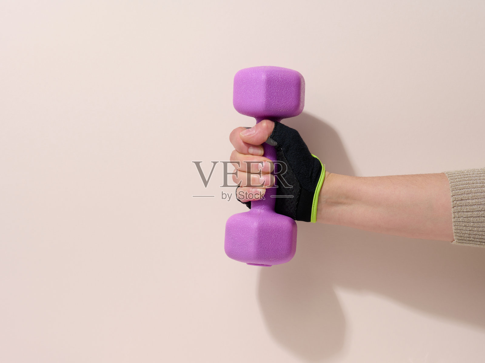 在米色背景下，一只戴着黑色运动手套的女性手拿着一个紫色的一公斤哑铃照片摄影图片