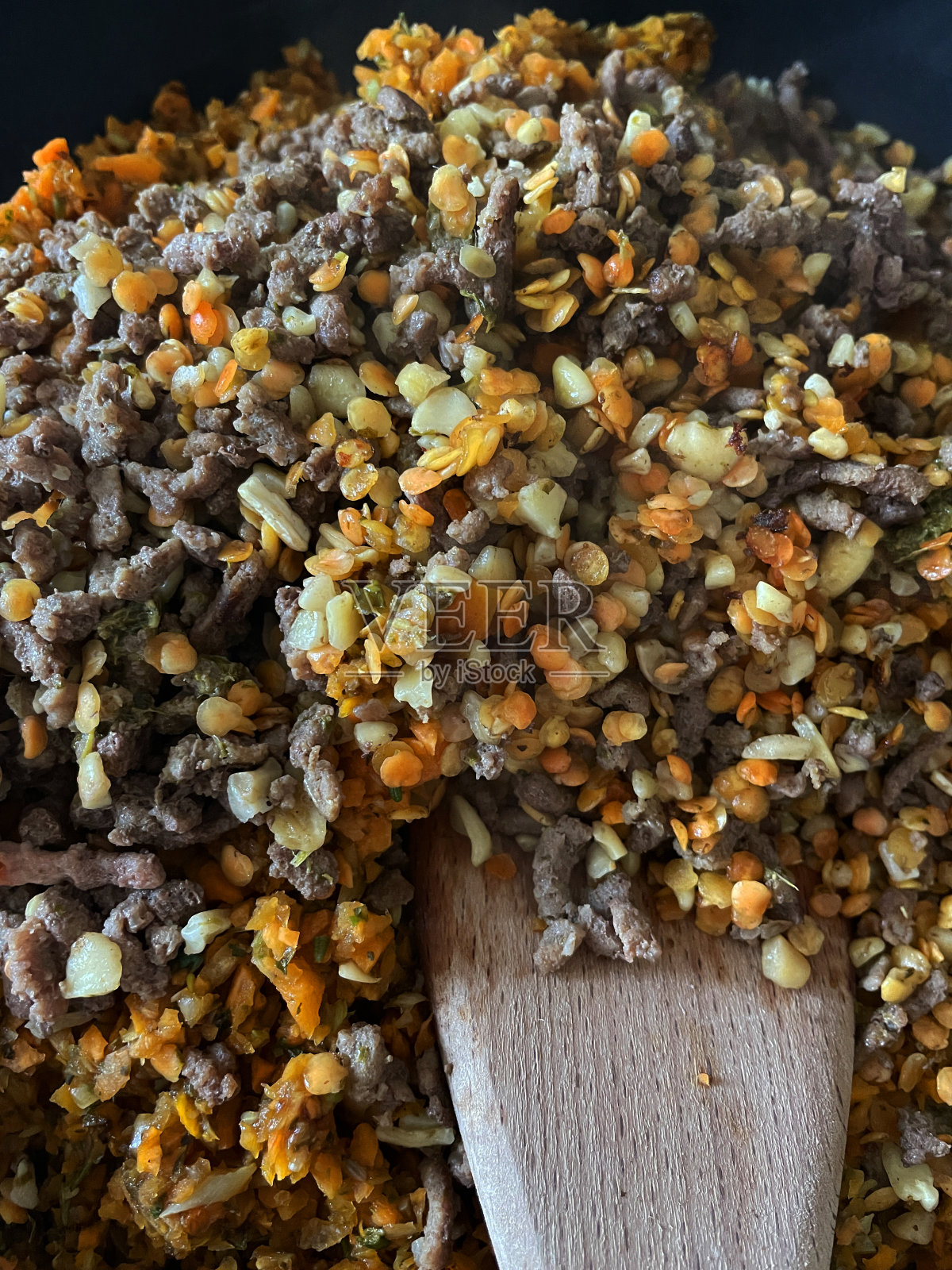 不粘锅包含半熟的瘦肉碎牛肉，碎肉与切碎的胡萝卜，洋葱，核桃和红扁豆一起褐变，准备肉酱，用木铲搅拌，升高视野照片摄影图片