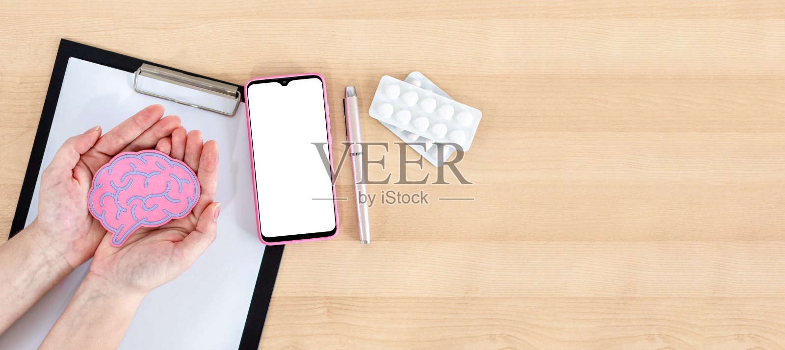 女性手持大脑模型、智能手机、剪贴板和药丸，在木桌上照片摄影图片