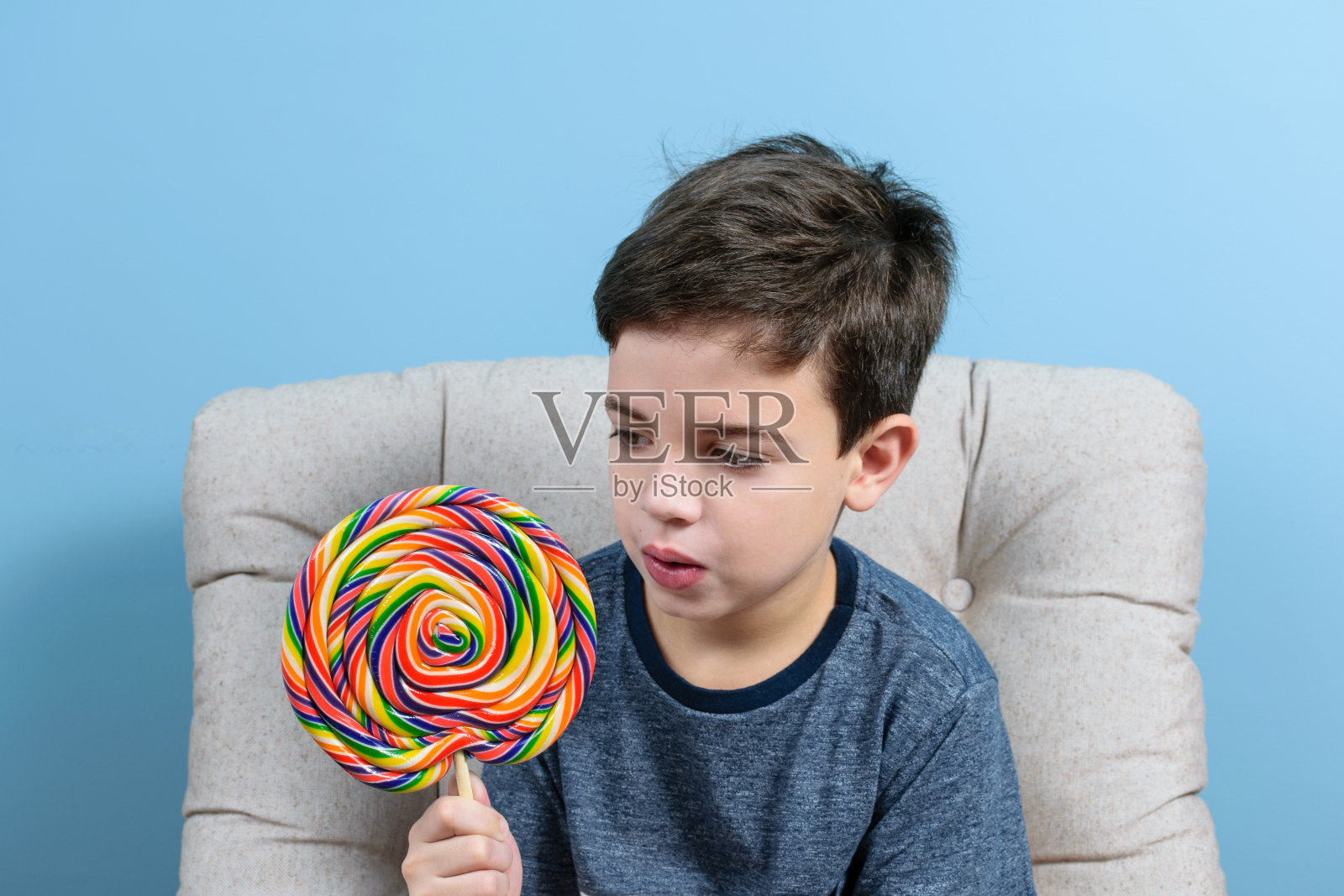 一个8岁的孩子在看一个彩色的大棒棒糖。背景是一面蓝色的墙。照片摄影图片