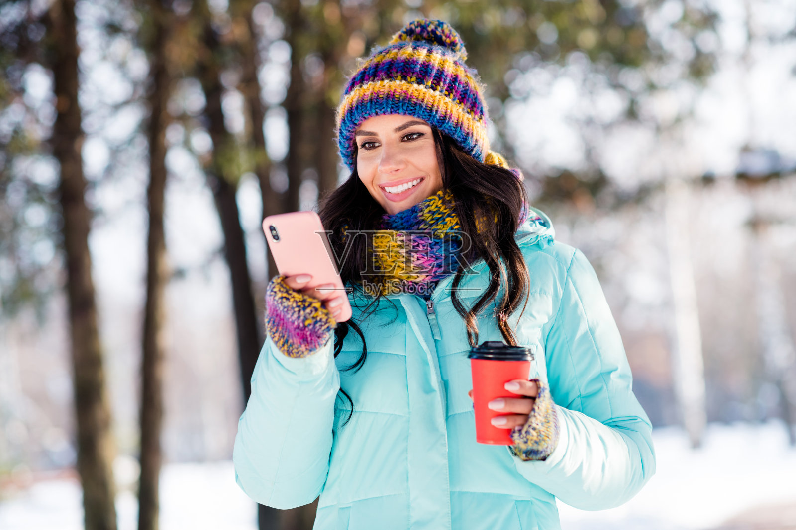 可爱的梦幻女士手持电话，外卖杯，喝茶，戴针织帽，围巾，外套在公园外面的照片照片摄影图片