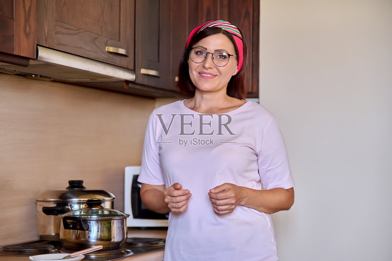 一位中年妇女在厨房里准备食物，脸上带着微笑照片摄影图片