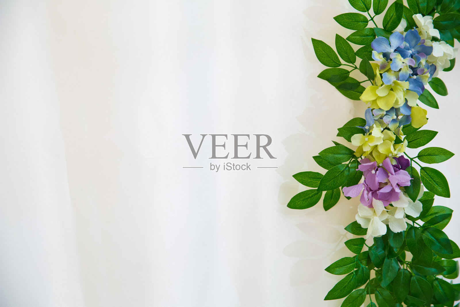 与面积的复制空间，文字，文字，图形设计。绿叶纹理的宏观细节。绿色的叶子和白色，粉红色，黄色，蓝色，人工花在白色的背景。照片摄影图片