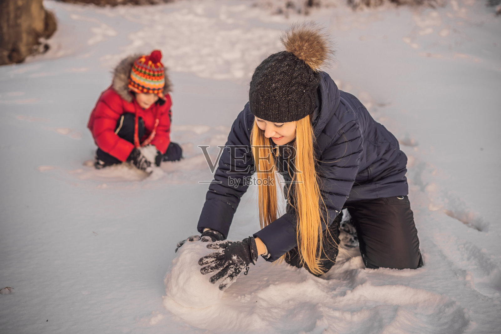 幸福的家庭穿着温暖的衣服。微笑的母亲和儿子在户外堆雪人。冬季活动的概念照片摄影图片