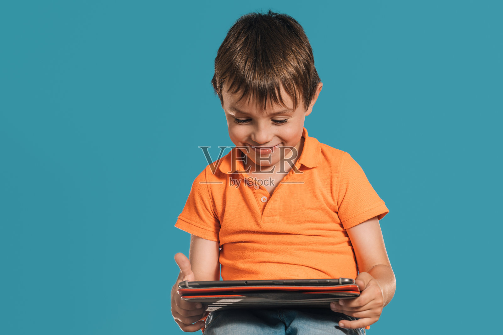 一个男孩在蓝绿色背景下玩平板电脑的特写镜头。照片摄影图片