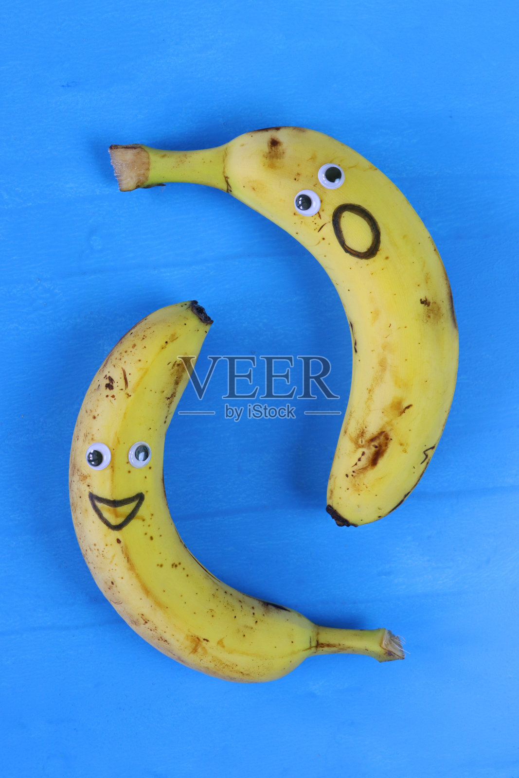 有趣的特写图像，卡通面孔在成熟的香蕉上，有大眼睛和嘴巴，笑脸和震惊的脸，蓝色背景，升高的视野，儿童健康饮食，幽默的概念照片摄影图片