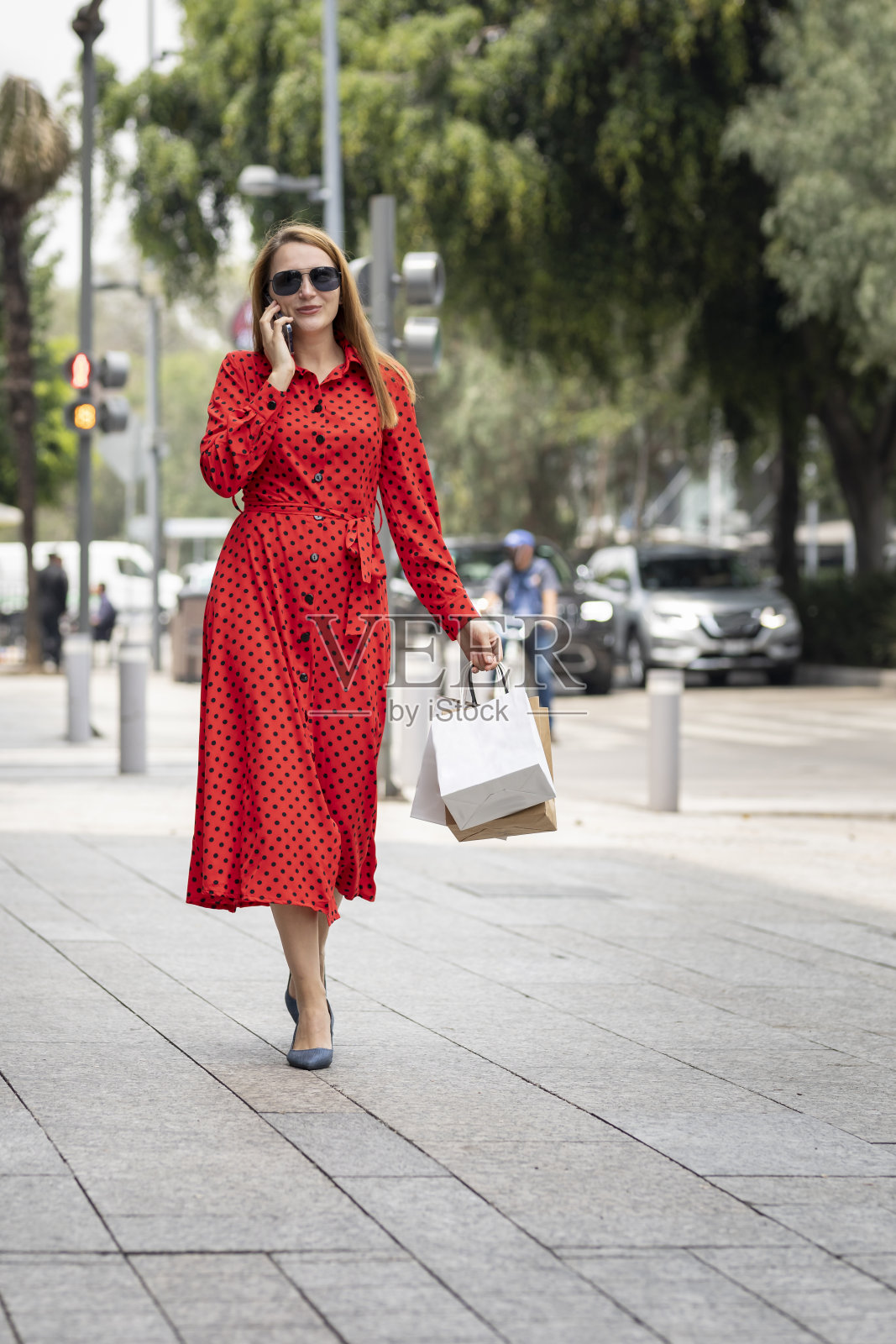 年轻快乐的白种女人穿着红色的衣服，拎着购物袋，时髦地走在街上照片摄影图片