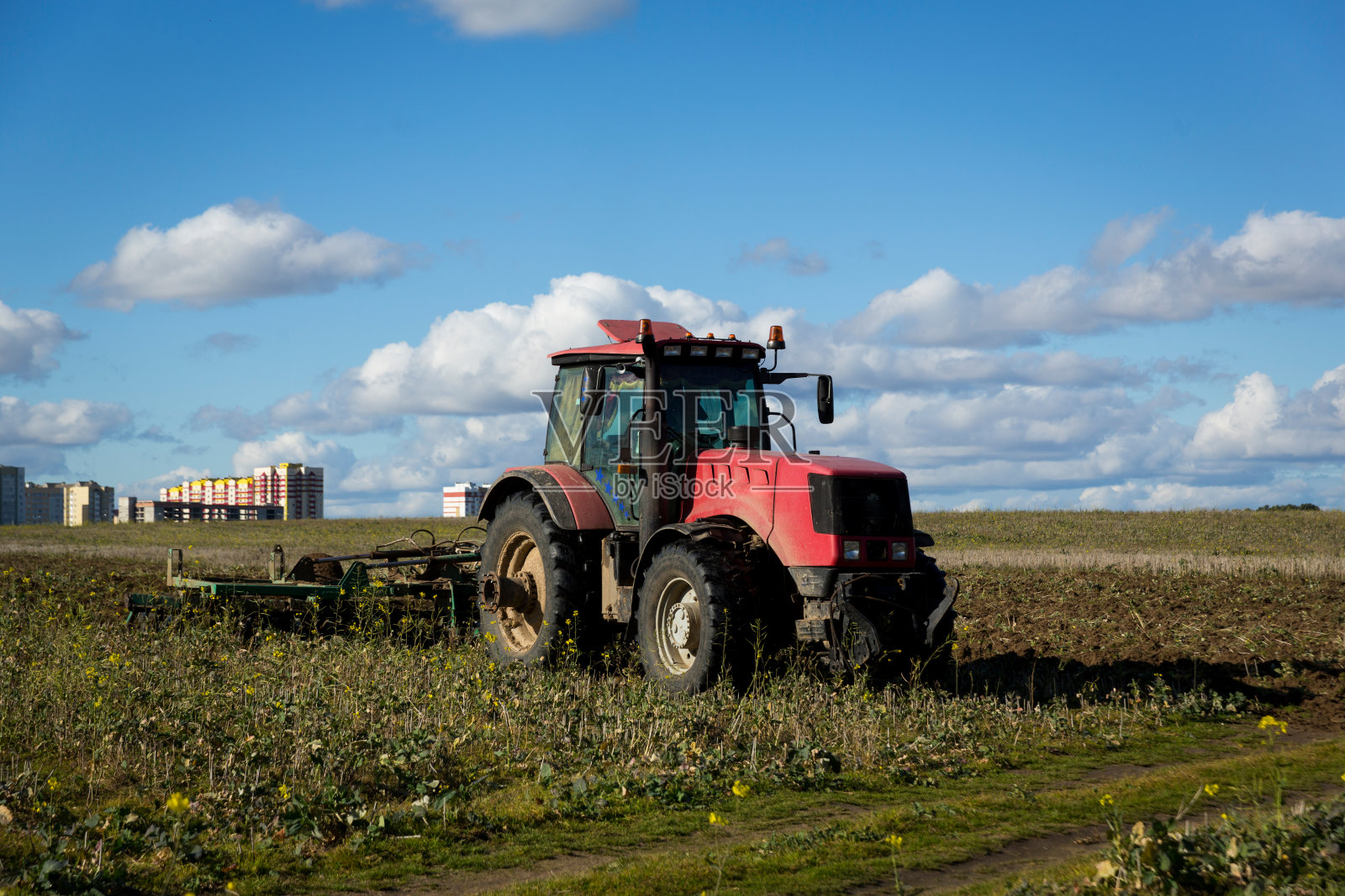 农民开着拖拉机(一种农业机械)，用耕耘机整地。田野里的现代红色拖拉机。一边用犁在田里耕作一边用重型拖拉机犁地。照片摄影图片