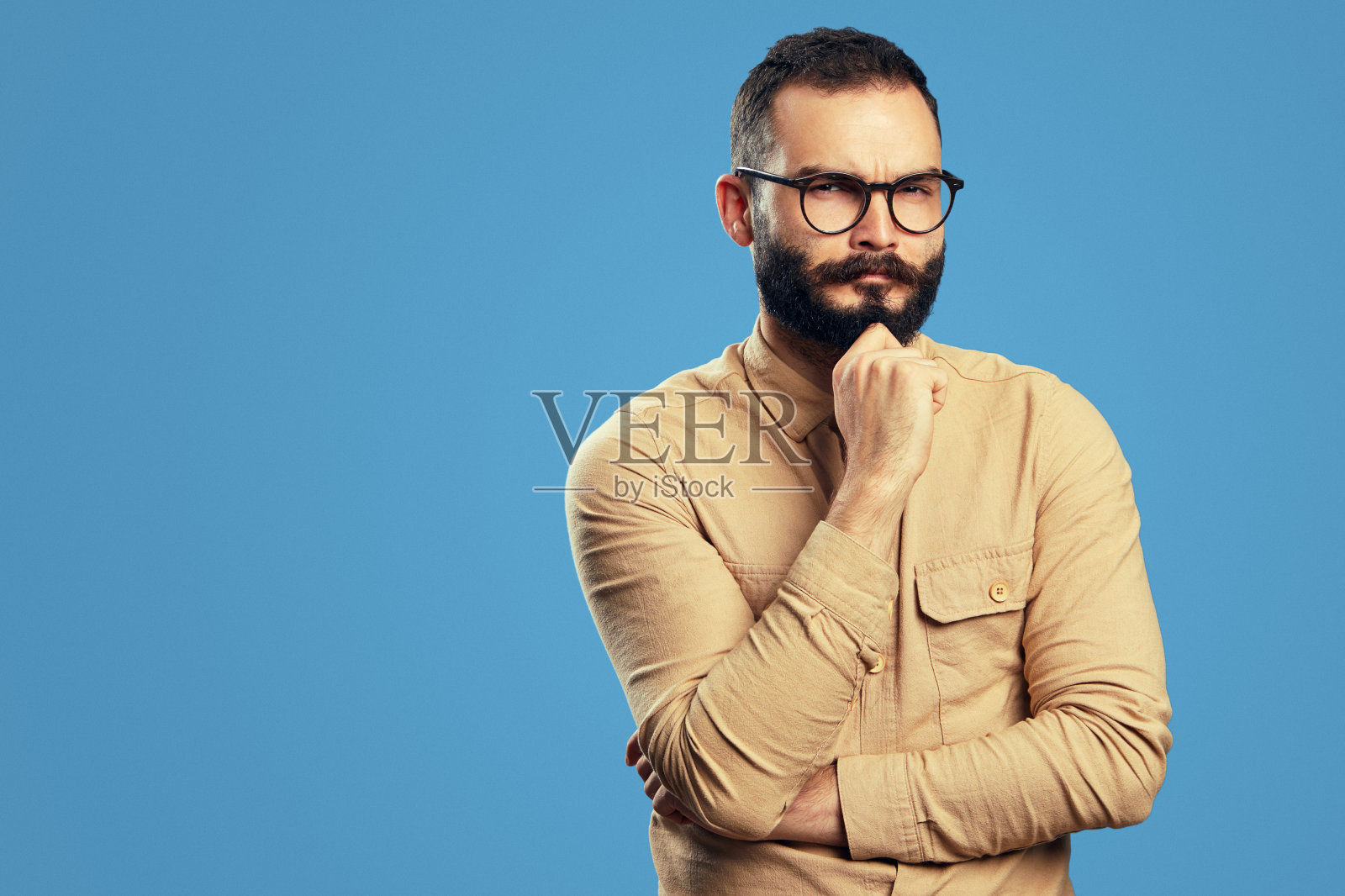 一个穿着米色休闲衬衫的人，摸着下巴，怀疑地看着镜头照片摄影图片