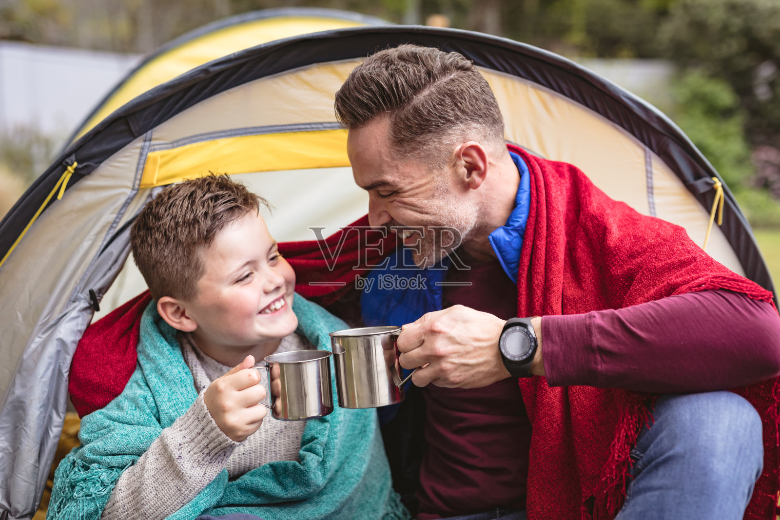 一对白人父子坐在花园的帐篷里，微笑着举杯喝咖啡照片摄影图片