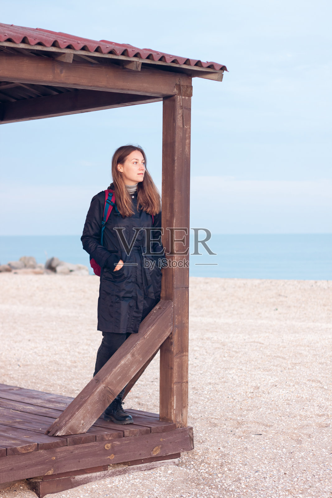 18、快乐年轻女子穿黑风雨衣空秋海边沙滩。微笑的女孩用热水瓶喝茶。生活方式照片摄影图片