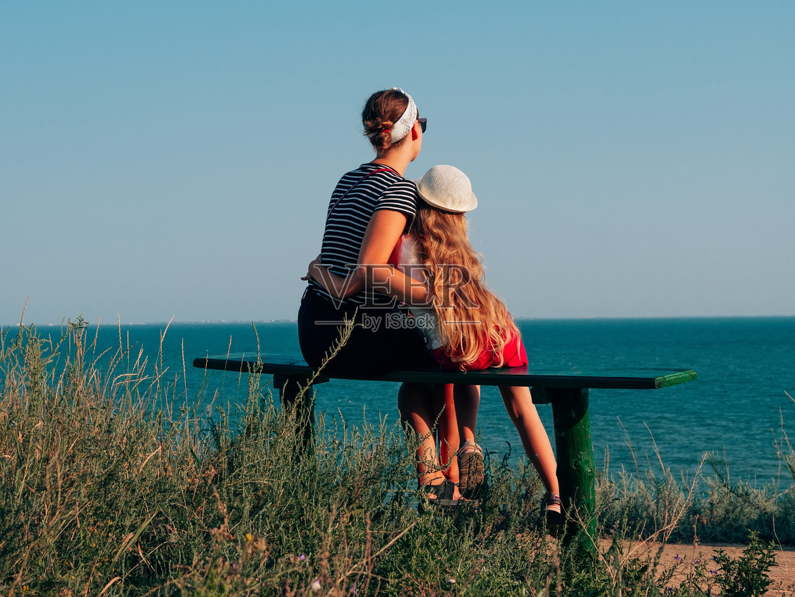 幸福的母女坐在长凳上欣赏海景。妈妈和孩子一起散步，很开心照片摄影图片