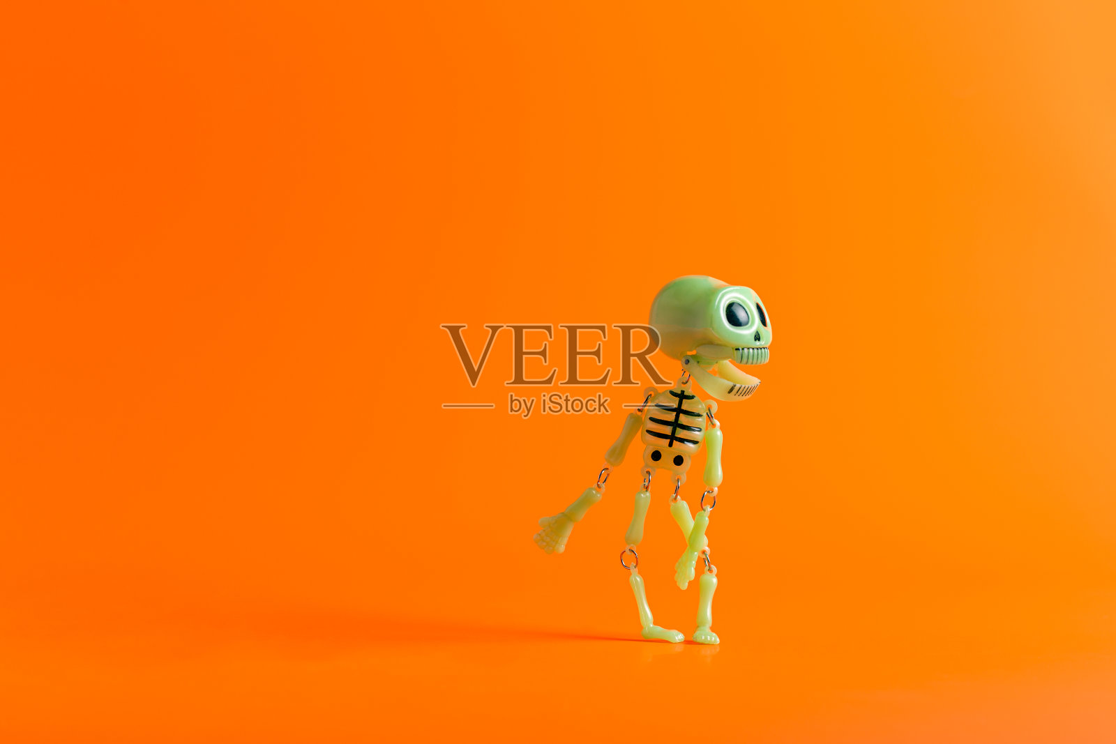 欢乐的玩具骷髅在橙色的背景与复制空间跳舞。万圣节派对的概念照片摄影图片