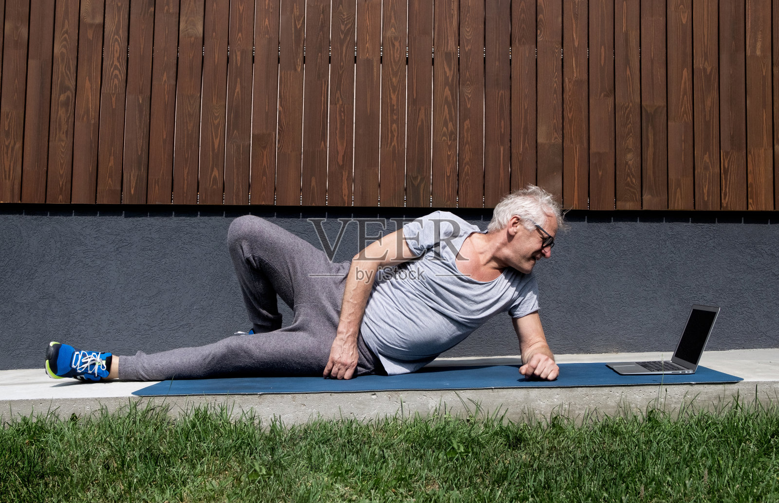 在一个温暖的夏日，一位身体健康、运动健硕的老人正在家里用笔记本电脑进行体育锻炼照片摄影图片