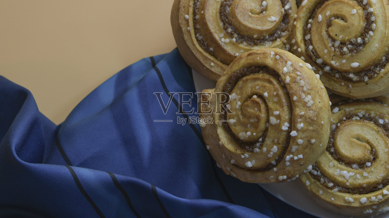 肉桂卷放在白色的盘子上，橙色和桃子的背景和蓝色的布料照片摄影图片