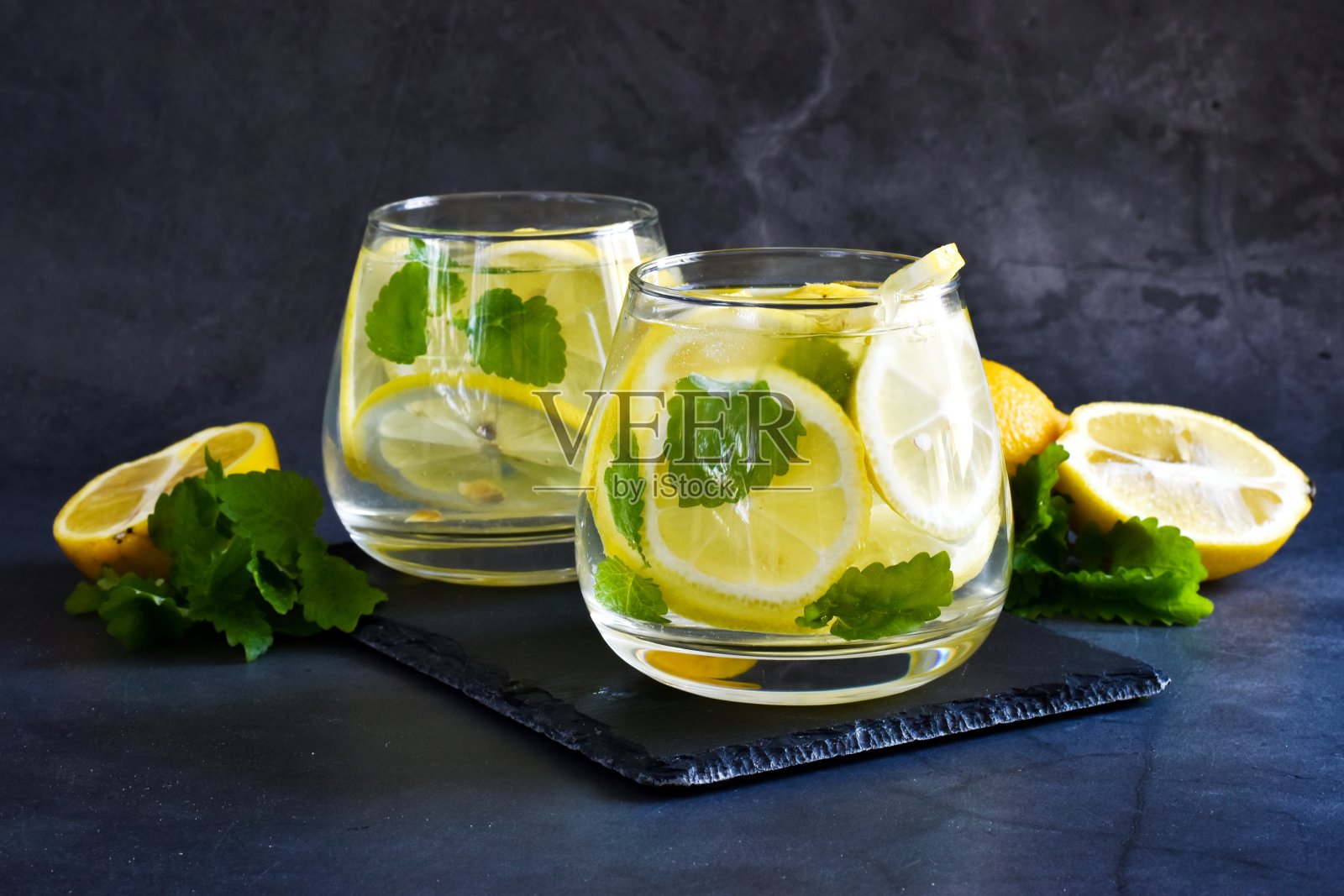 两杯柠檬水或莫吉托加柠檬和薄荷的鸡尾酒，在灰色背景的黑色板上清凉的饮料。副本的空间。照片摄影图片