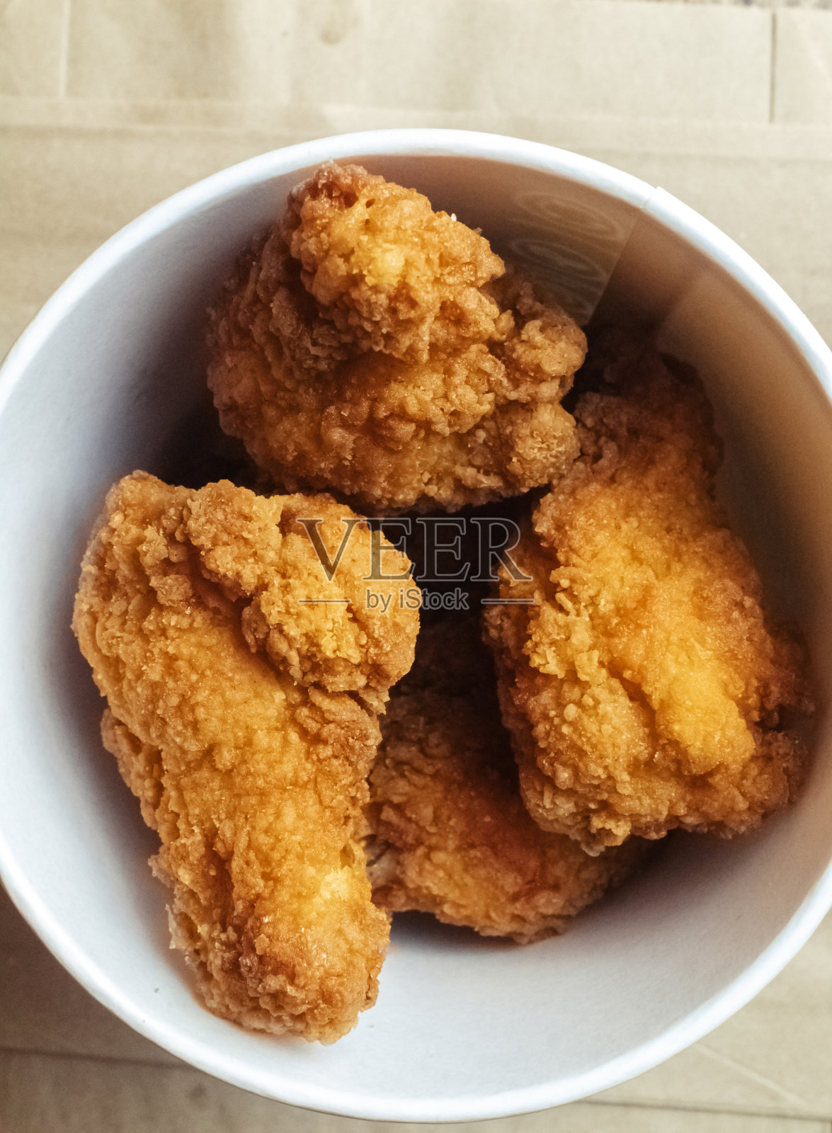 面糊炸鸡翅的特写镜头。在一家快餐店里，桌子上有一纸盒鸡肉和酱汁。阳光美丽地落在拿着食物的女孩的手上照片摄影图片