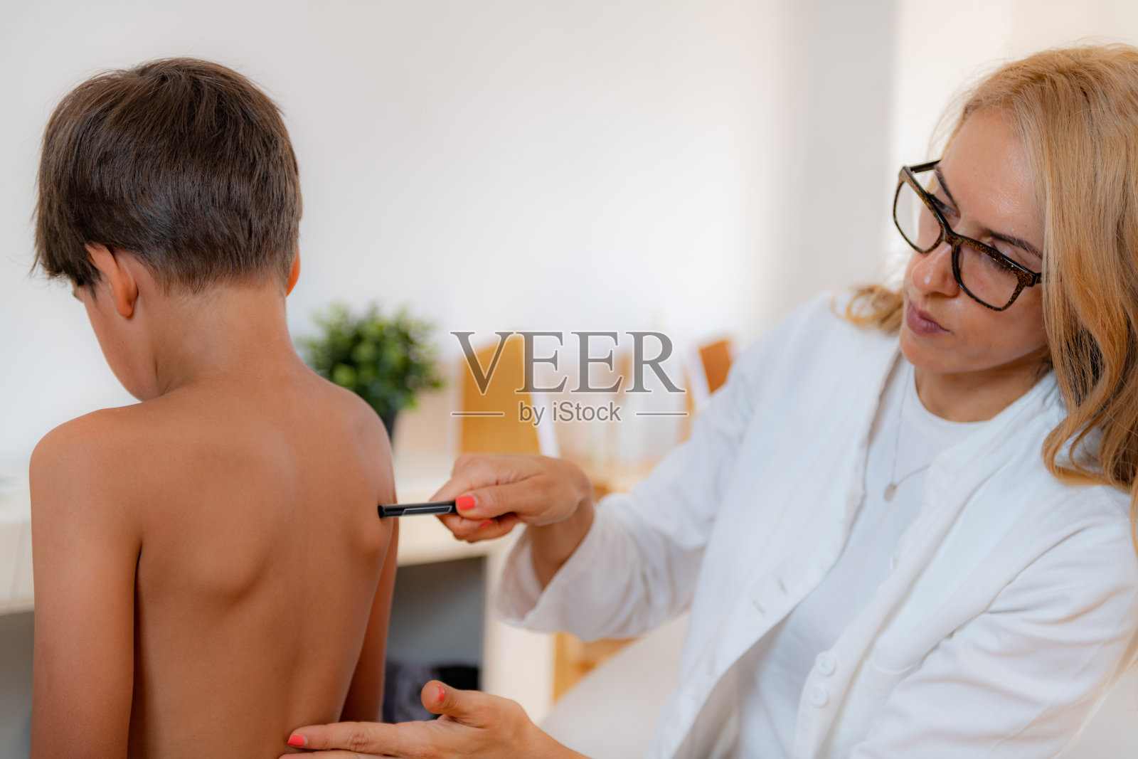 儿科医生检查一个男孩的姿势，在他的背上做记号，检查肩胛骨的角度。照片摄影图片