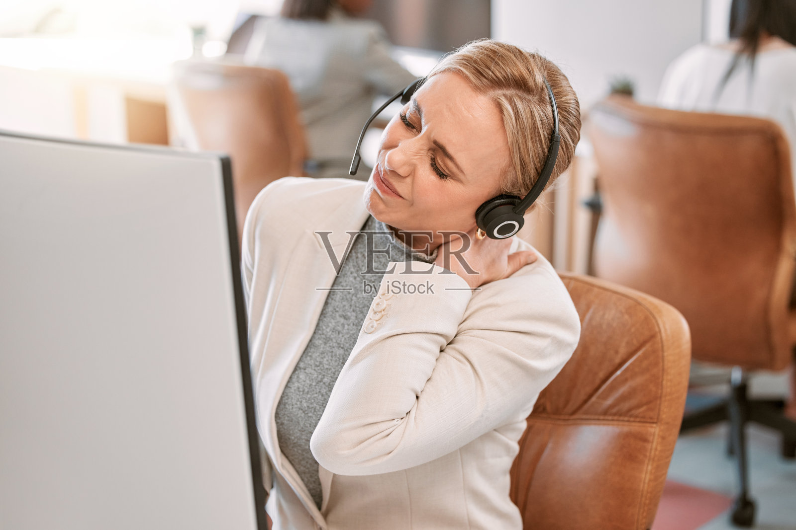 一个迷人的成熟女性呼叫中心代理遭受脖子疼痛，而工作在她的电脑在办公室照片摄影图片