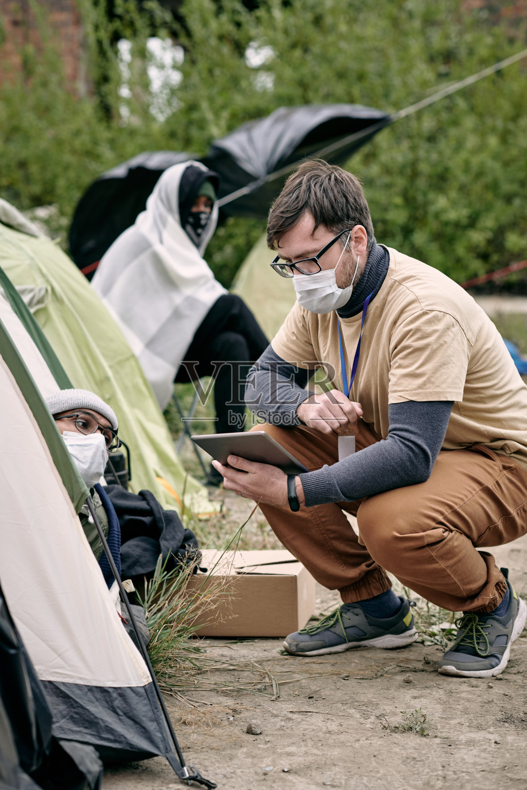 拿着平板电脑的志愿者蹲坐在一个难民帐篷旁照片摄影图片