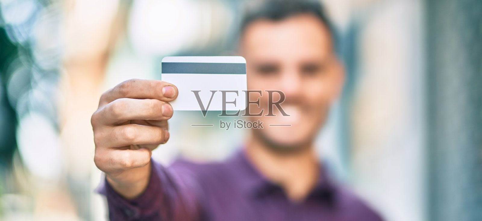 年轻的西班牙人微笑着快乐地持有信用卡在城市。照片摄影图片