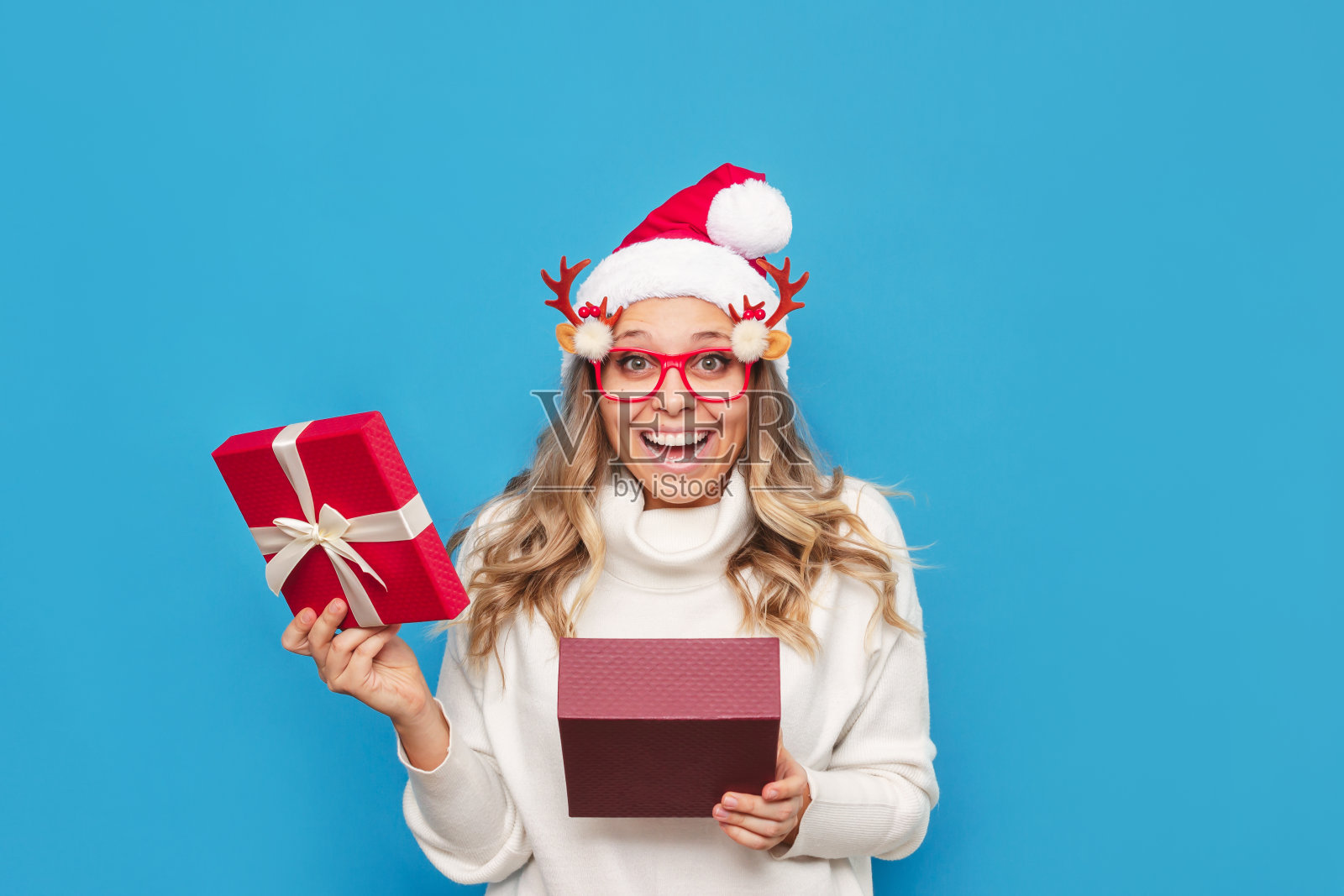 一位身穿白色保暖毛衣、头戴红色圣诞帽的年轻女子对收到的礼物感到很高兴。圣诞节和新年的概念照片摄影图片