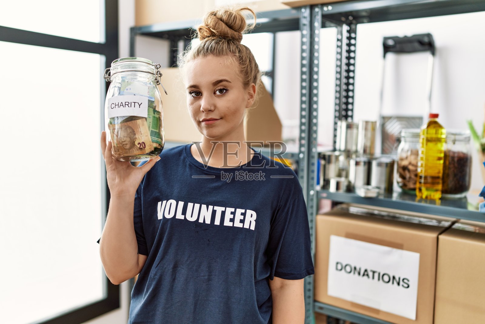 一名年轻的白人女子拿着装有钱的慈善坛子站在捐款台上思考的态度和冷静的表情看起来很自信照片摄影图片