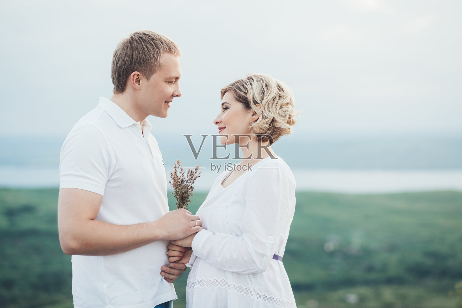 年轻的白人怀孕女孩穿着白色背心裙，戴着花圈。一对已婚夫妇在等待孩子的出生。概念是婚后生活。照片摄影图片