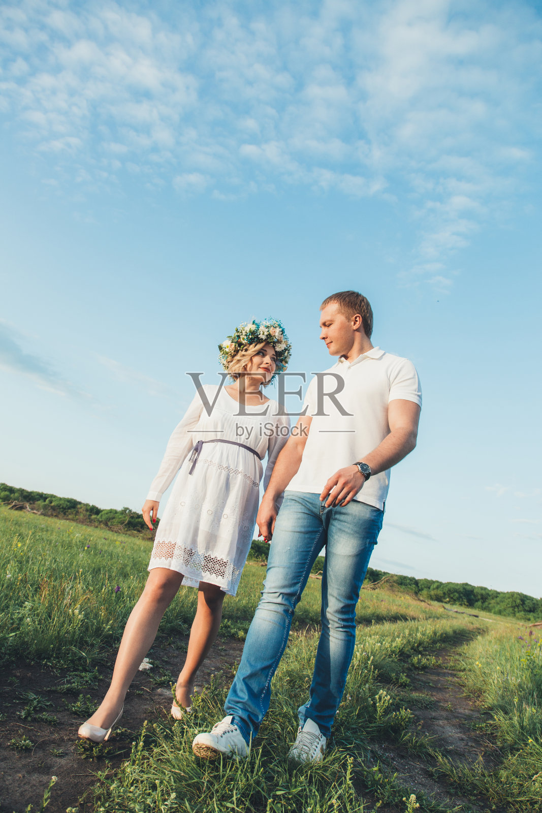 年轻的白人怀孕女孩穿着白色背心裙，戴着花圈。一对已婚夫妇在等待孩子的出生。概念是婚后生活。照片摄影图片