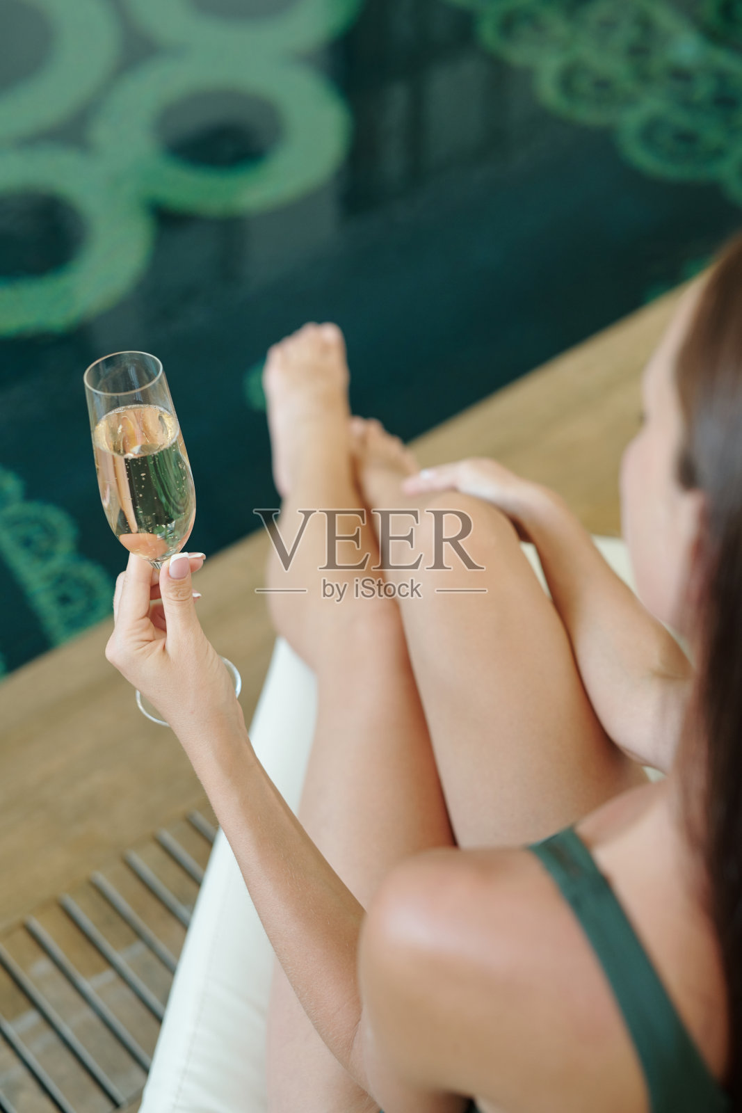 年轻女子手持香槟，坐在泳池边照片摄影图片