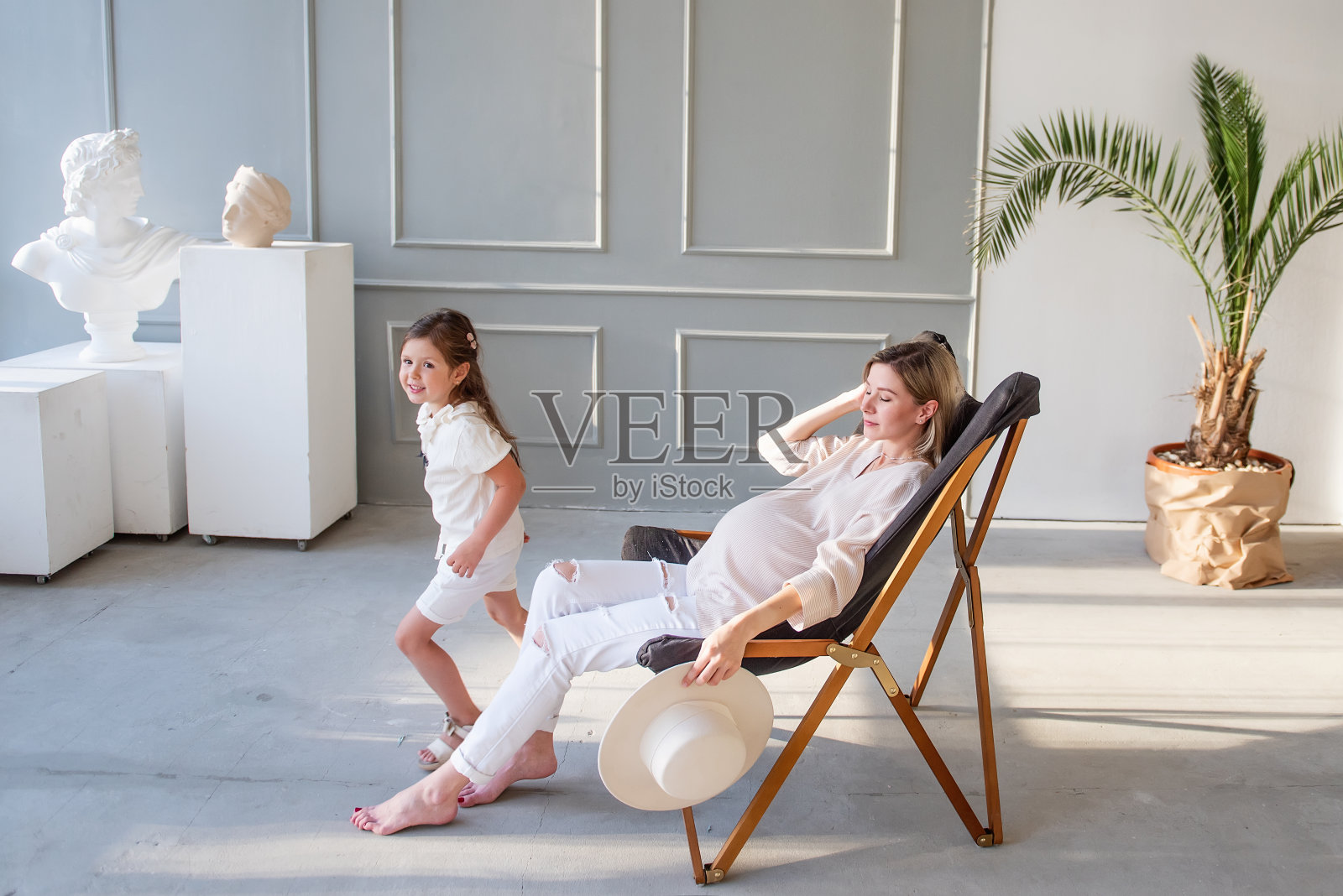 一位怀孕的母亲坐在木制躺椅上，拥抱、亲吻她的大女儿。照片摄影图片