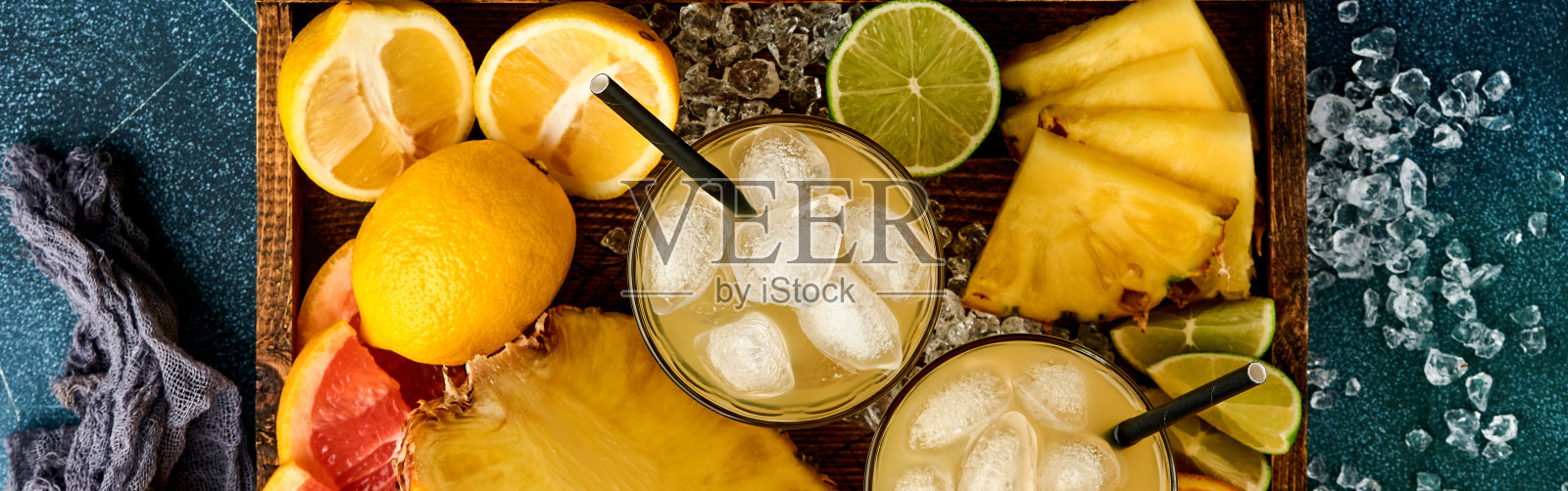 新鲜的菠萝汁配以冰和各种颜色成熟的热带水果切片，葡萄柚，橘子，酸橙，柠檬，平铺构图，在深蓝色的石头背景上。模拟。照片摄影图片