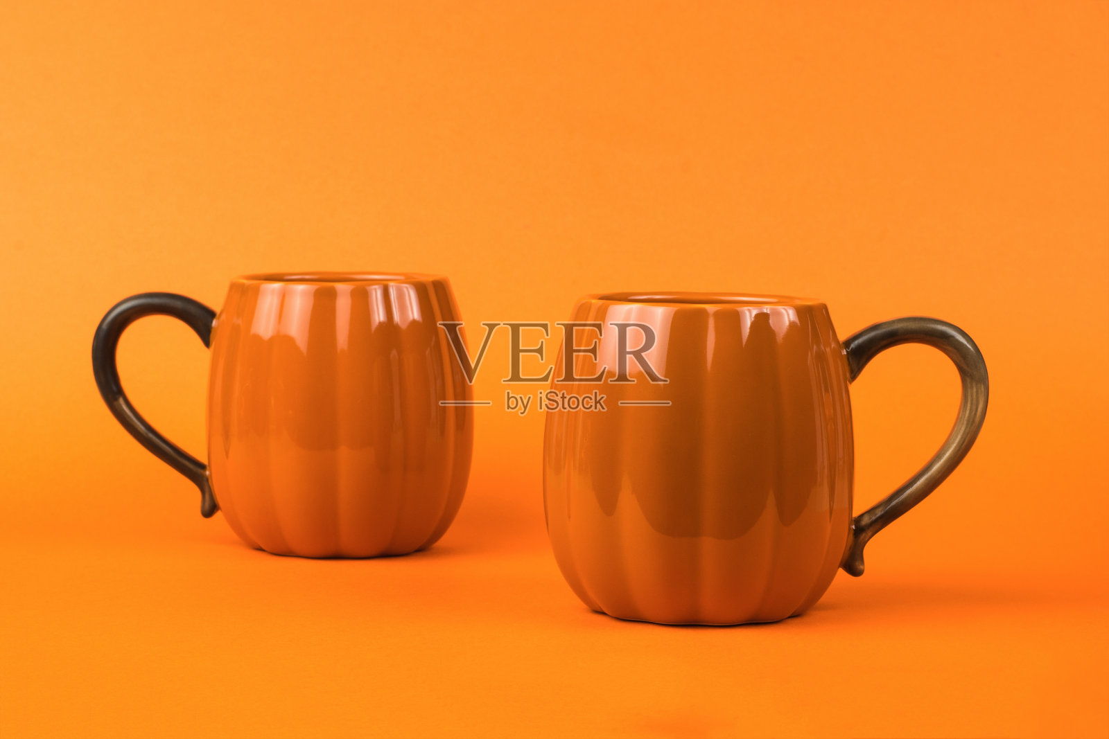 两个橙色南瓜形状的杯子，背景是橙色的。照片摄影图片