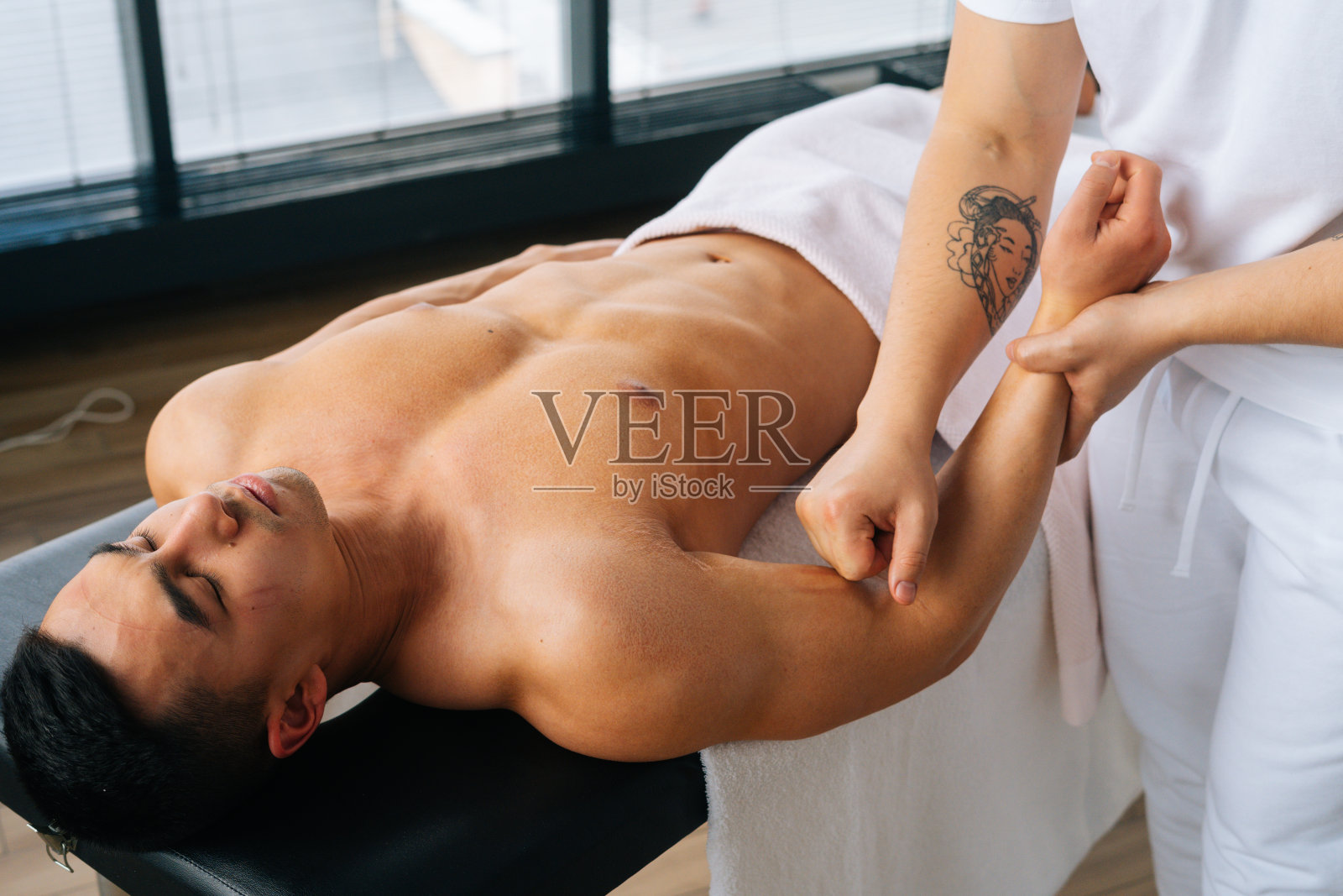 专业男按摩师在体育锻炼后，用有力的双手按摩肌肉发达的运动员的前臂照片摄影图片