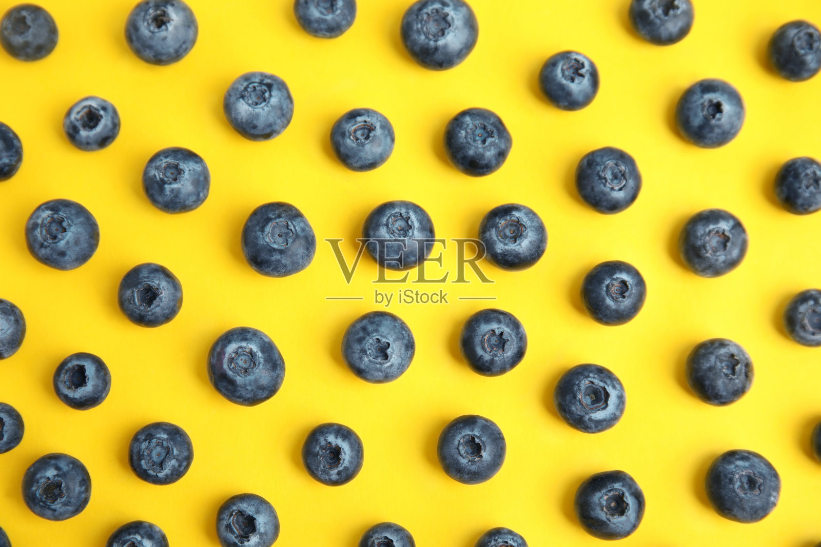 新鲜成熟的蓝莓放在黄色的背景上，平躺着照片摄影图片