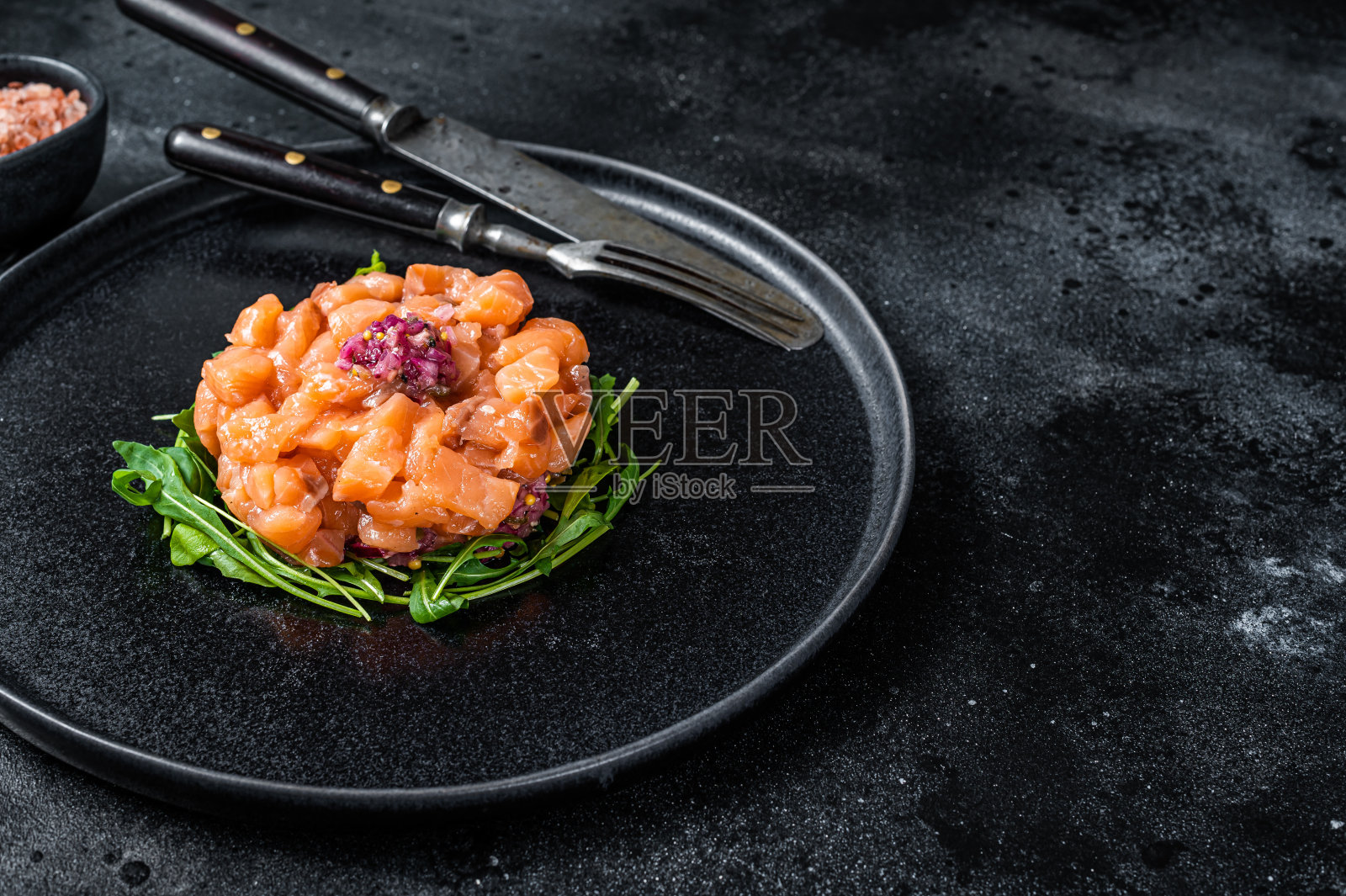 生鲑鱼鞑靼或鞑靼与红洋葱，芝麻菜和刺山柑在黑色盘子。黑色背景。前视图。本空间照片摄影图片