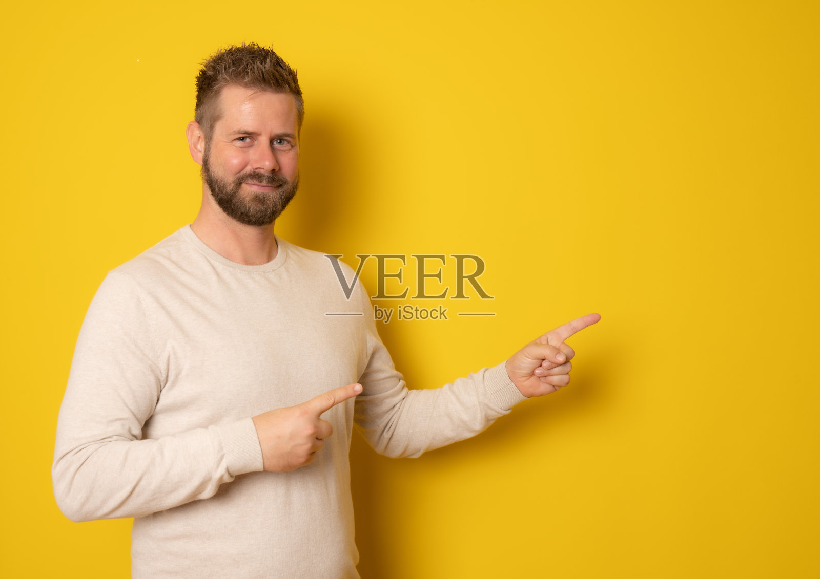 一个快乐的大胡子男人的肖像，手指指向在黄色背景上孤立的副本空间照片摄影图片