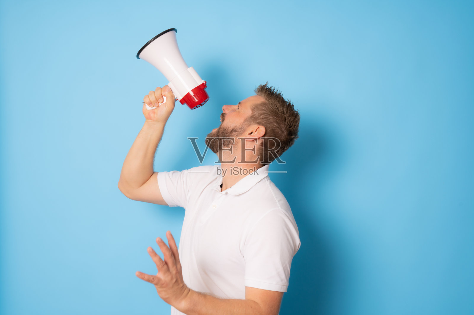 一个英俊的男人隔着一堵蓝色的墙，通过扩音器大喊照片摄影图片