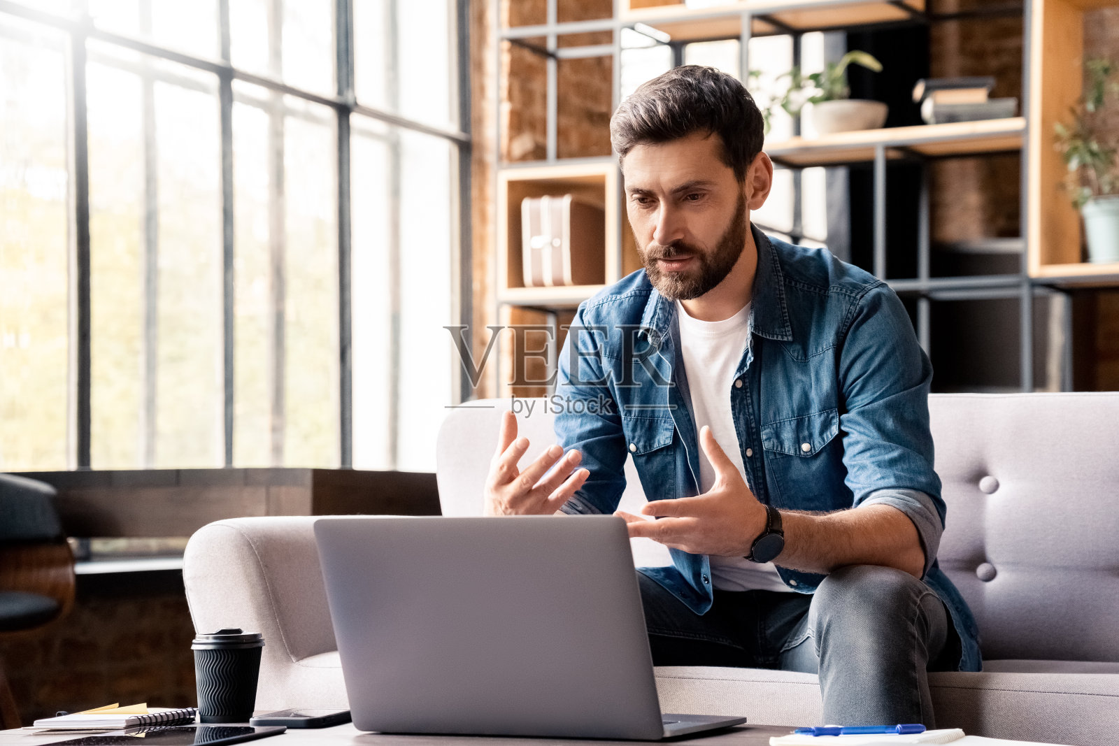 男人一边说一边看着笔记本电脑屏幕，在家里的办公室里开视频会议照片摄影图片