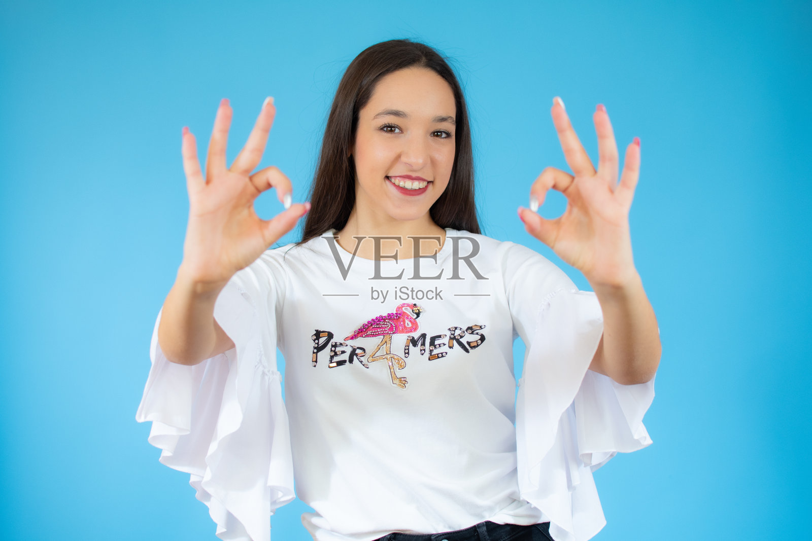 一个快乐的年轻女人在蓝色的背景上用手指展示着ok的标志照片摄影图片