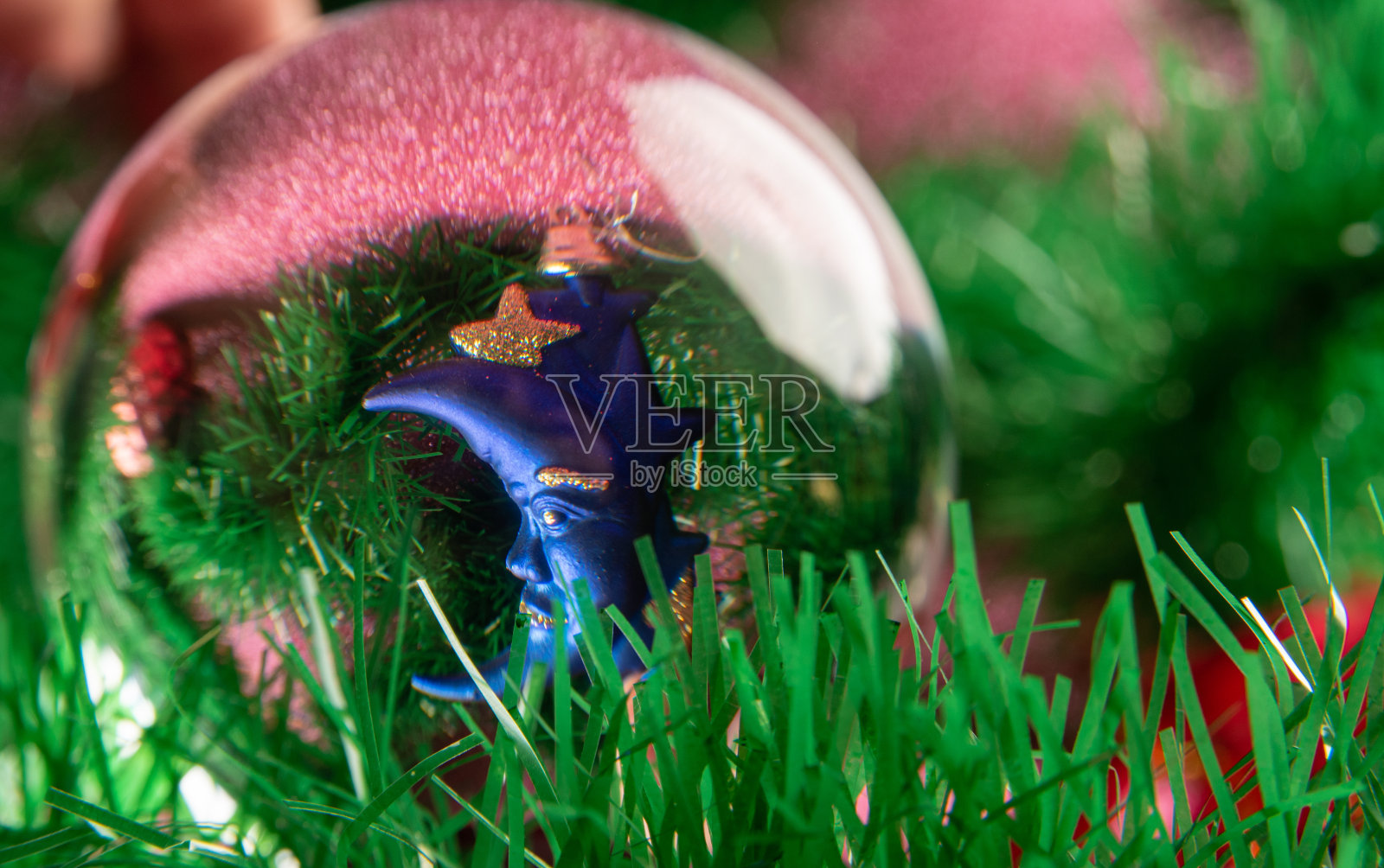 塑料和闪闪发光的圣诞装饰品通过一个透镜球在粉红色的闪闪发光的表面。有选择性的重点。照片摄影图片