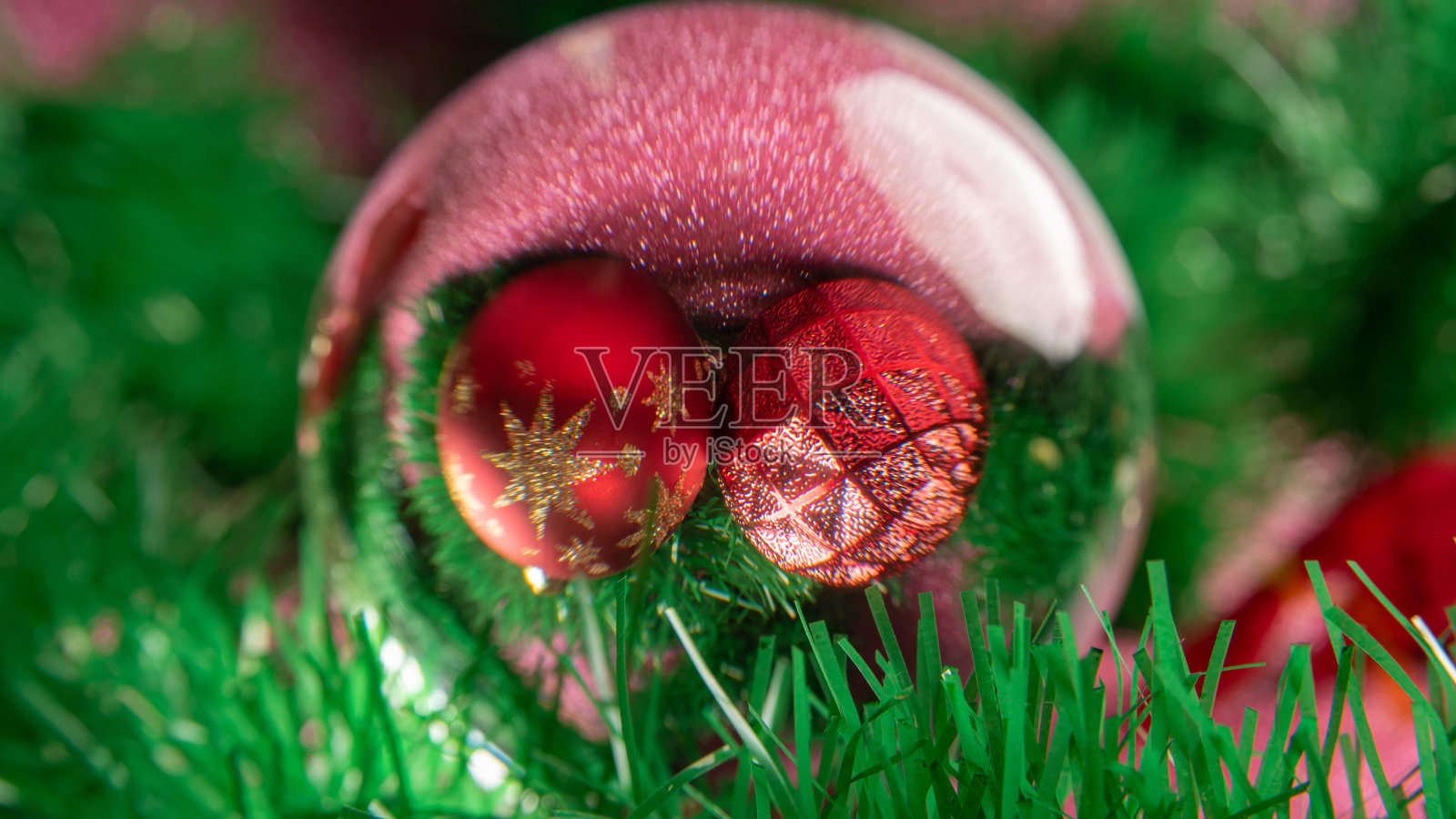 塑料和闪闪发光的圣诞装饰品通过一个透镜球在粉红色的闪闪发光的表面。有选择性的重点。照片摄影图片