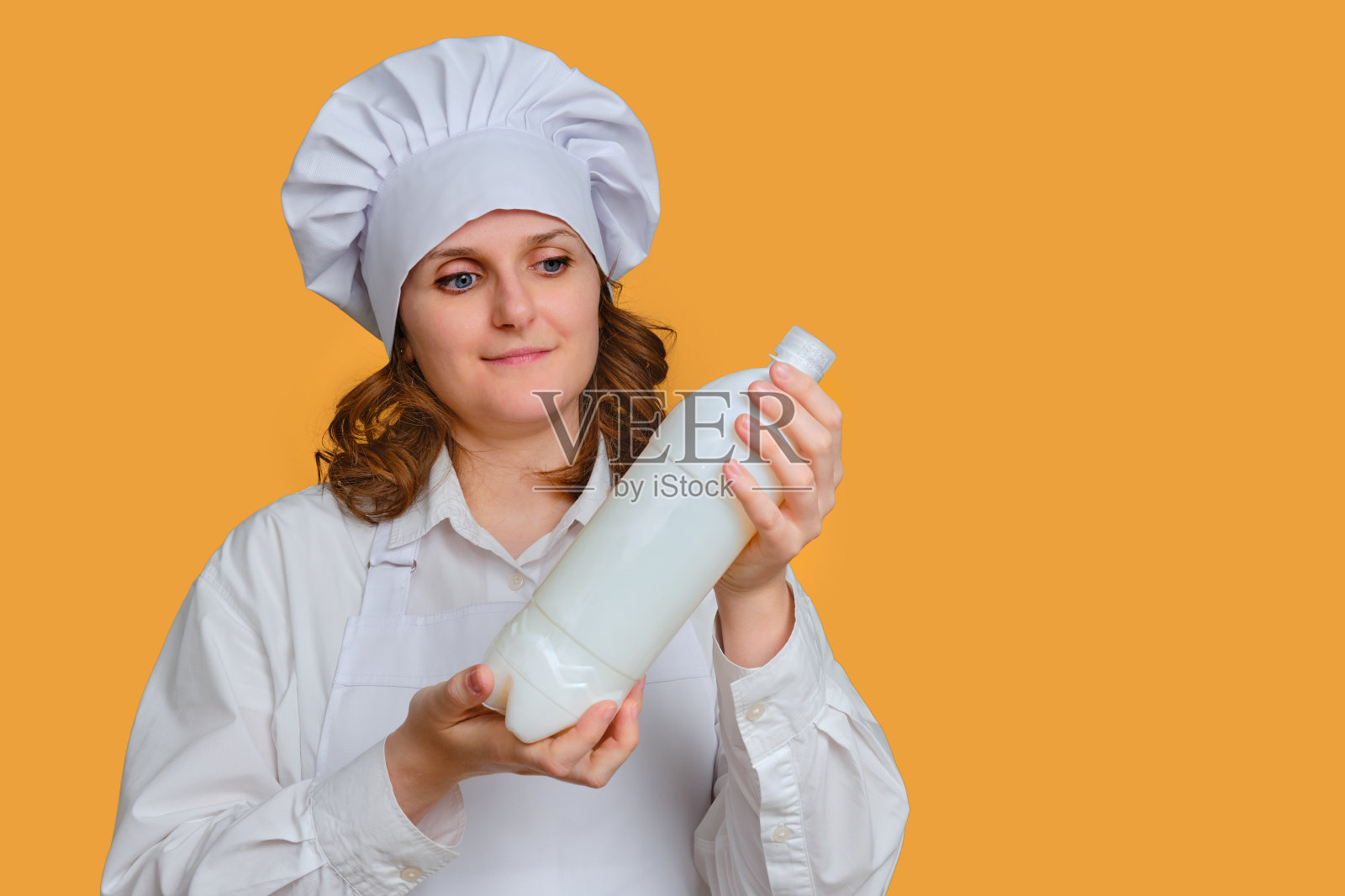 一个女厨师在黄色的工作室背景下，手里拿着一瓶塑料牛奶照片摄影图片