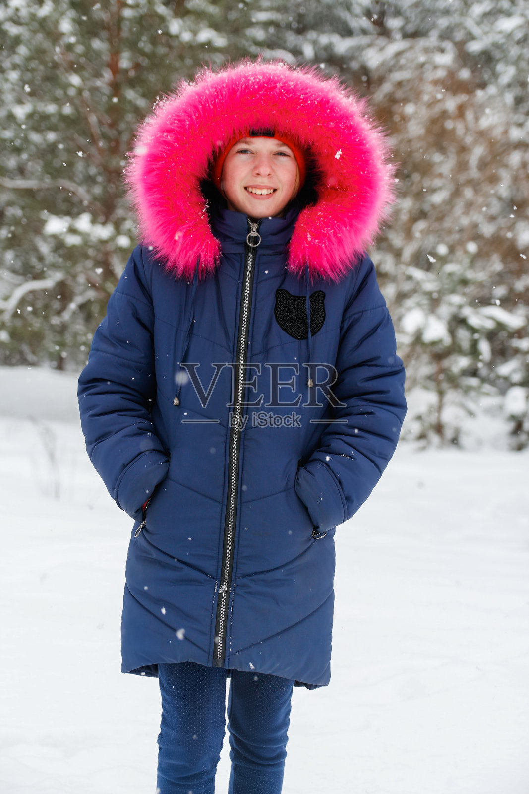 纵向肖像的十几岁牙齿微笑的女孩在明亮的粉红色温暖的帽外在自然冬天下雪的森林背景。漂亮的孩子在室外微笑，寒冷的天气。白人小孩，10岁照片摄影图片