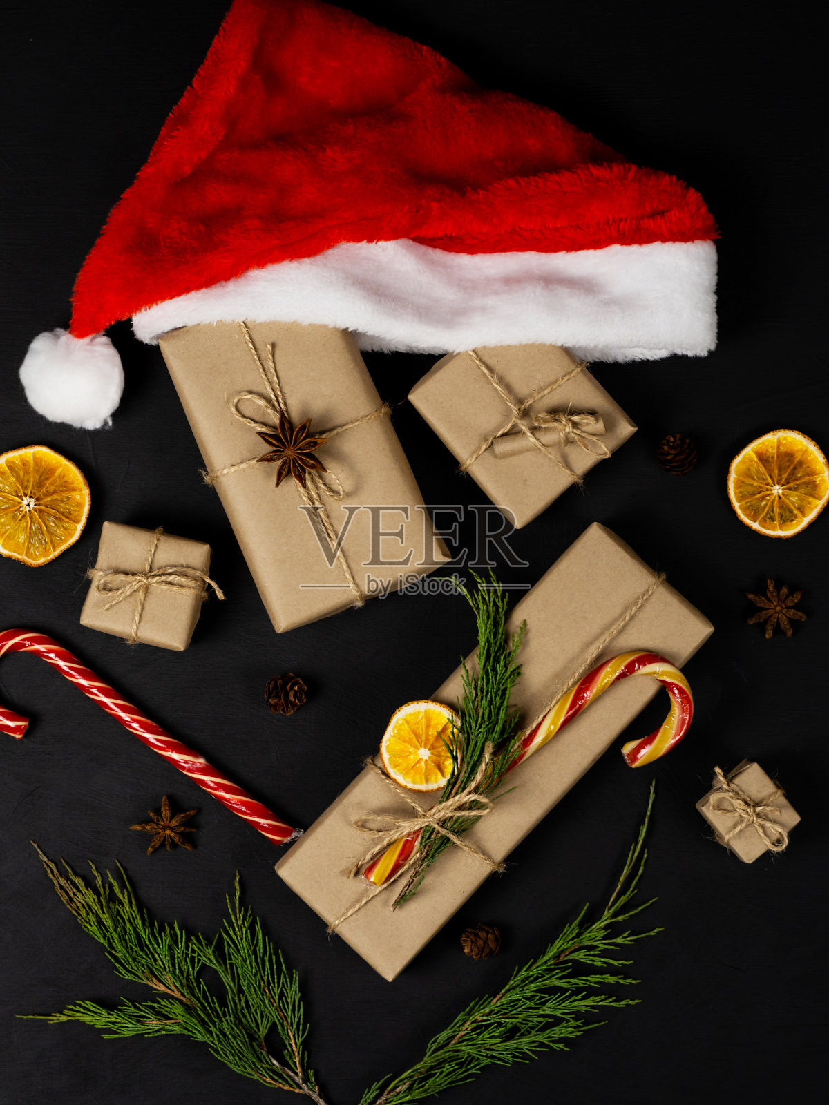 圣诞老人的皮帽。圣诞组成。云杉树枝，礼盒，糖果，黑色背景的圆锥体。圣诞节、新年概念。照片摄影图片